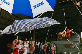 At a family farm in Bridport, Dorset, England, an aerial artist performs in a hanging ring during the reception, as guests with umbrellas look on.